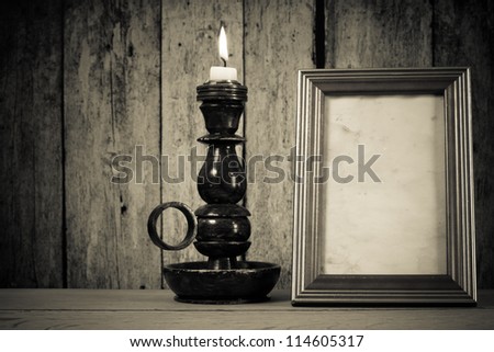 Candlestick with burning candle and photo frame on the table in front of wooden wall background