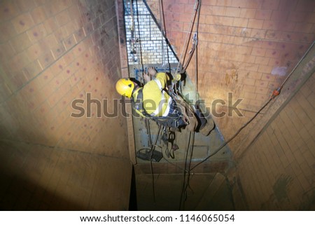 Picture of rope access miner abseiling down hanging in fall arrest position commencing using solid square tool  measurement metal wall at construction site Perth, Australia  
