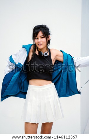 A studio portrait of a young and attractive Chinese Asian millennial teenager in sporty clothing. She is shrugging as she is smiling at the camera. 