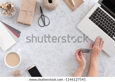 Top view of woman hands holding credit card on modern fashion background, business concept, online shopping, workspace with laptop, mobile phone, gift box, cup of coffee and notebook, flat lay.