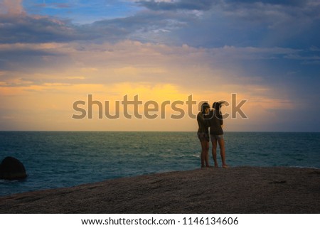 Two women standing at the sea in the evening