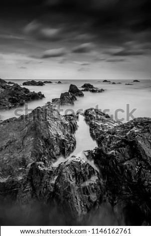 Long exposure seascape and rocky beach in black and white. Nature composition. A slow shutter speed was used to see the movement ( Soft focus due to long exposure shot ).