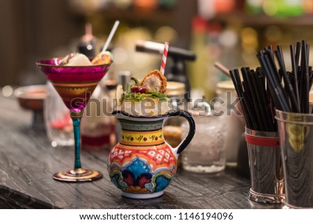 Fancy cocktails in red patterned wineglass and original painted jar are standing on bar counter with cocktail tools and ingredients. Modern trendy alcoholic drinks in club. Party background concept. Royalty-Free Stock Photo #1146194096