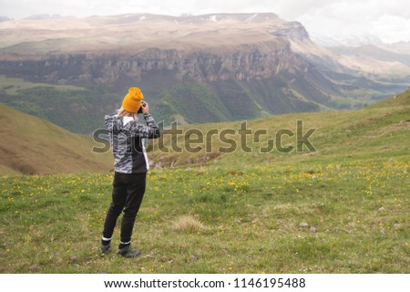 A young girl takes pictures of a plateau on top of a high mountain on a cloudy day. View of the girl behind