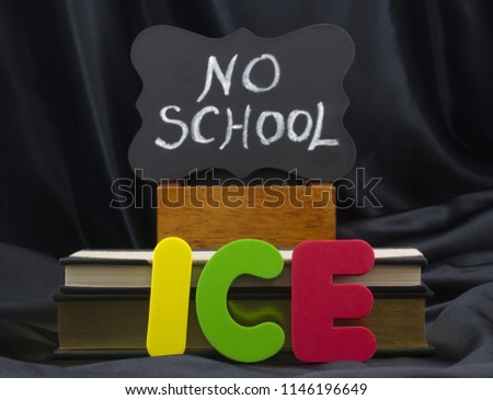 ICE in letters with NO SCHOOL on small chalkboard with books and black satin background. Icy weather conditions create danger and school closings.