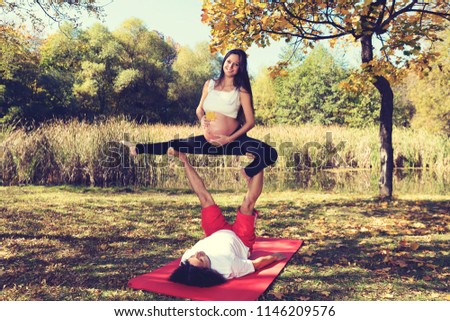 Autumn yoga in the park Man and pregnant woman doing acro yoga. Selective focus