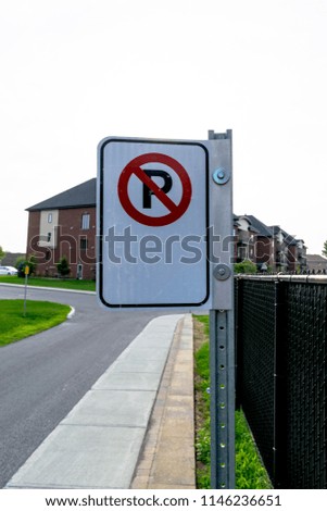 A no parking sign on the side of the road with a black fence and a building in the background