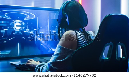 Shot of the Beautiful Pro Gamer Girl Playing in First-Person Shooter Online Video Game on Her Personal Computer. Casual Cute Geek wearing Glasses and Headset. Neon Room. eSport Cyber Games Internet Royalty-Free Stock Photo #1146279782