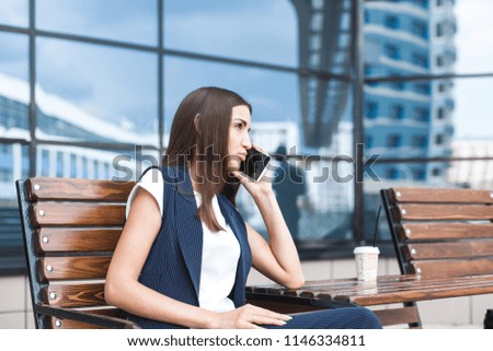 business lady in a suit is sitting at a table with a notebook, a cup of coffee and a mobile phone, against a background of glass buildings