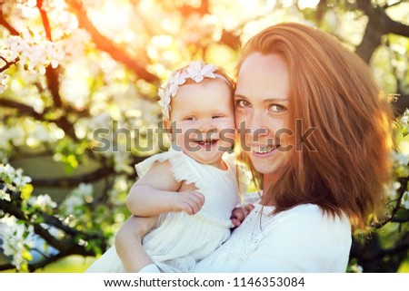 little baby on hands of mother. woman playing with child outside in blooming spring garden. portrait of family of two people. happy family concept. spring landscape background. apple trees in blossoms
