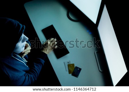 Hacker in mask under hood having many credit cards in computer room - with copy space on blank screen to insert text ,word, and pictures