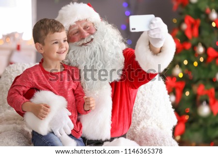 Authentic Santa Claus taking selfie with little boy indoors