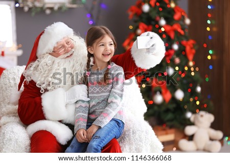 Authentic Santa Claus taking selfie with little girl indoors