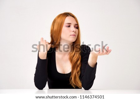portrait of a beautiful girl with red hair on a white background with different emotions. She sits at the table in front of the camera and shows different emotions in different poses