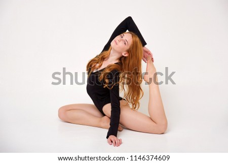 portrait of a beautiful girl with red hair on a white background doing stretching gymnastic. She is right in front of the camera smiling and looking happy