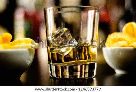 glass of whiskey with ice cubes and salty snacks on the background of the bar, party time