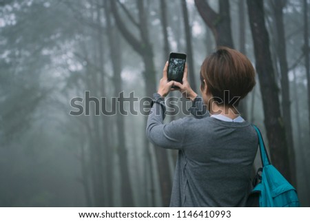 female traveler photographing with mobile phone and enjoying a beautiful nature forest. 