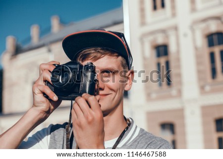 Close up portrait of handsome hipster man with beard, in stylish hat and glasses posing with retro camera and backpack stands on wooden background. cap, street photo, film, lens, outdoor portrait