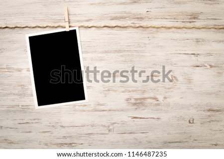 Blank photo frame hanging on rope on wooden textured background