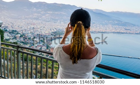 Young Girl travelerand  taking picture ,  viewing Alanya city panorama and beaches from the viewpoint of the mountain: "Alanya Kalesi". concept of travel and tourism