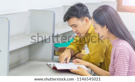 Two students reading book and doing homework together and helping each other sitting in a table at home with library