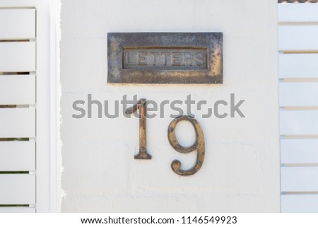 Close up of aged metallic house number "19" and letter box sign on white pillar.