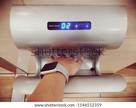 Sport woman dries wet hand in modern vertical hand dryer in public restroom. Top view