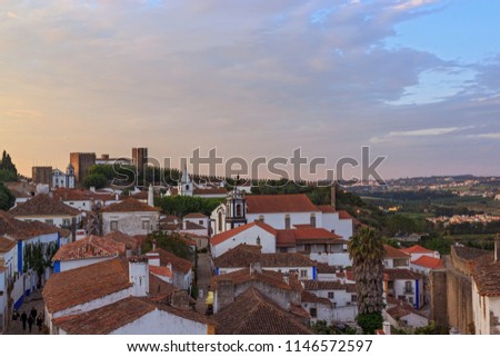 View of narrow streets and castle of Obidos from wall of fortress. Scenic old town with medieval architecture in the sunset. White houses red tiled roofs. Popular touristic destination.