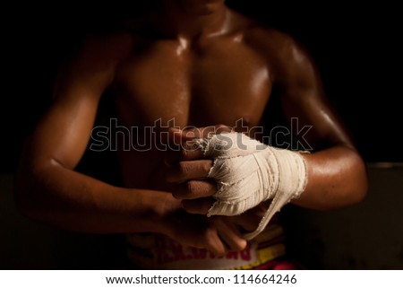 The muscular fighter tying tape around his hand preparing to box