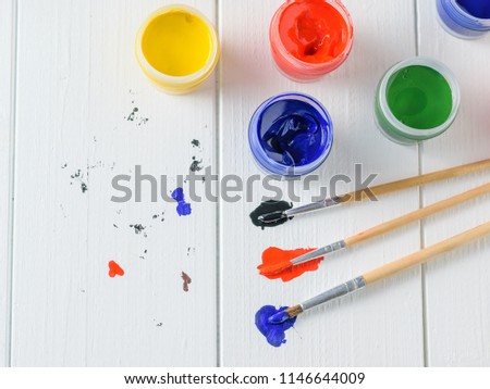 Multi-colored brushes and jars of paint on a white wooden table. Creative kit. Flat lay.
