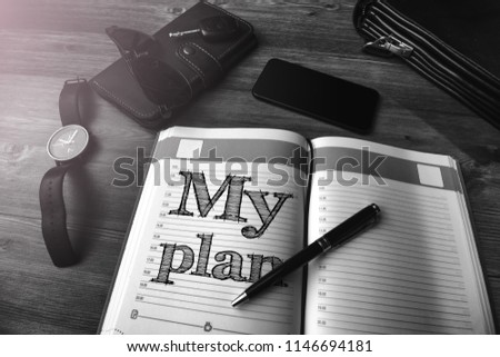Men's accessories (bag, keys, purse, notebook and glasses) on a wooden table with text My plan