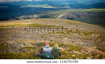 Atmospheric moment for lovers in the mountains.Hiking woman and man with backpack is sitting on the top of the mounting and looking at a beautiful landscape. Travel Lifestyle and survival concept rear
