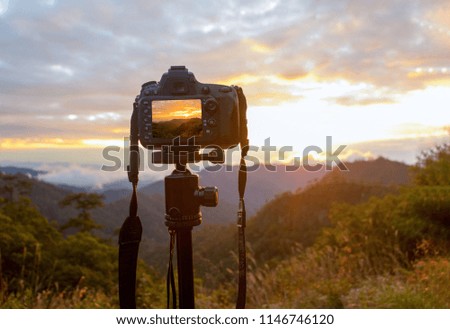 A DSLR camera  on tripod. It is on mountain. Photography on sunset and mountain
