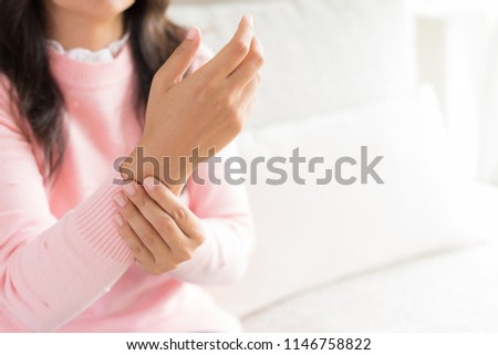 Closeup woman sitting on sofa holds her wrist hand injury, feeling pain. Health care and medical concept.