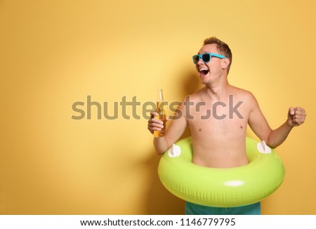 Shirtless man with inflatable ring and bottle of drink on color background
