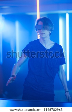Handsome Teenage Boy Wearing Virtual Reality Headset Dances. In the Background Cool Neon Retro Lights.