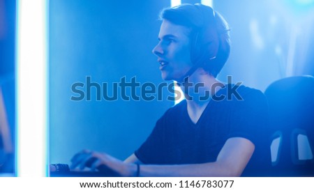 Shot of the Pro Gamer Playing in Video Games on His Personal Computer. Talking with His Team through Microphone on Headphones. Retro Neon Room.