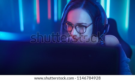 Beautiful Friendly Pro Gamer Girl Does Video Game Gameplay stream, Wearing Headset Talks / Chats' with Her Fans and Team into Headphones Microphone.Teenagers Having Fun. Background Neon Retro Colors.