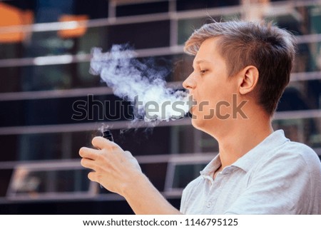 young handsome man in a white shirt smokes a vape on a modern background