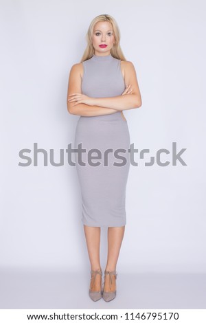 studio portrait in full growth of a young blond woman in a gray business midi-dress.