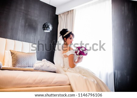 A charming bride with a red of flowers sits on the bed