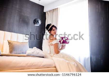 A charming bride with a red of flowers sits on the bed