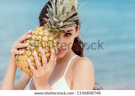 portrait of attractive girl in bikini holding fresh pineapple near the sea