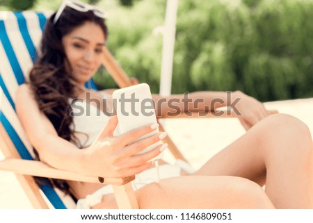 selective focus of woman taking selfie on smartphone while relaxing on beach chair on resort