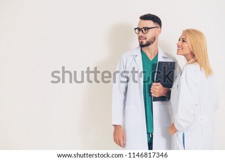 Confident surgical doctor holds document clipboard while standing with another doctor on white background. Medical service and healthcare people concept.