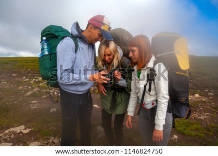 Hiking man and women with backpack enjoys a hike  and looks at the pictures taken on  camera in the mountains in the background a green floor and cloud. Photographer traveler on  high mountaint. Wande