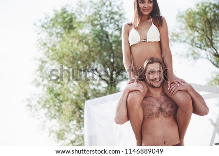 Happy young man wearing his wife on the shoulders of the beach.