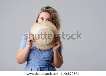Young blonde woman embarrassed and hides behind a straw hat. Shows only the eyes