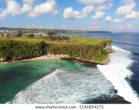 Aerial view of an amazing nature scenery with rock cliff on sandy coastline. Beautiful sea water with waves for surfing in summer season in Bali. Beauty Indian ocean landscape, holiday destination