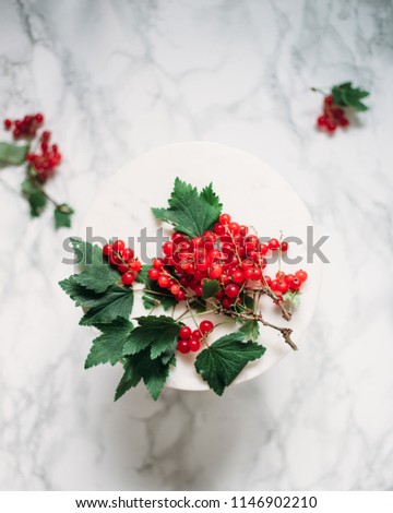 Red currant in a bowl, berries and leaves scattered on marble table